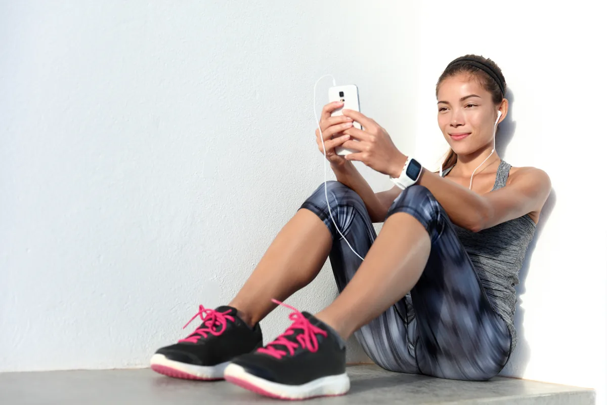 Une femme assise sur le sol en tenue de sport qui regarde son téléphone