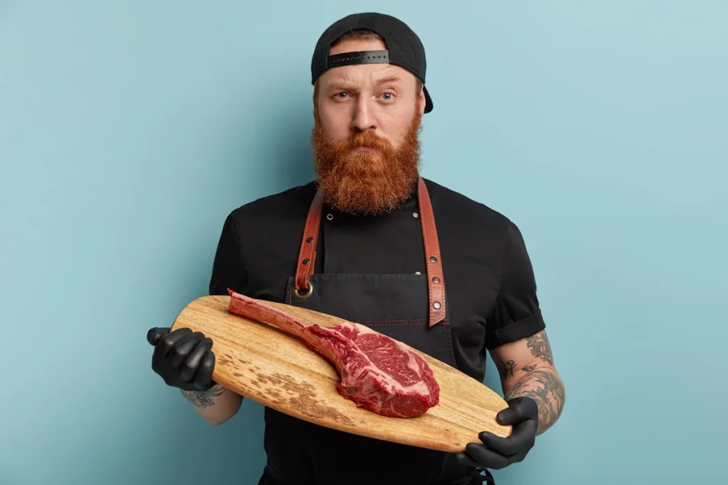 Un homme qui tient un plateau en bois avec une pièce de viande