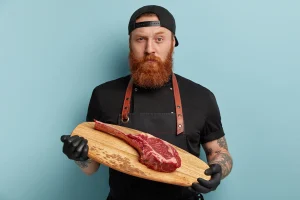 Un homme qui tient un plateau en bois avec une pièce de viande
